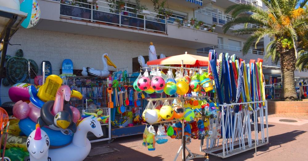 An outdoor shop filled with beach toys and inflatables. There are toy shovels, inflatable balls, and beach umbrellas.