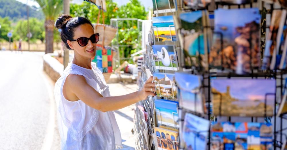 A woman spinning a product carousel with postcards at a gift store. The postcards show scenic landscape views.