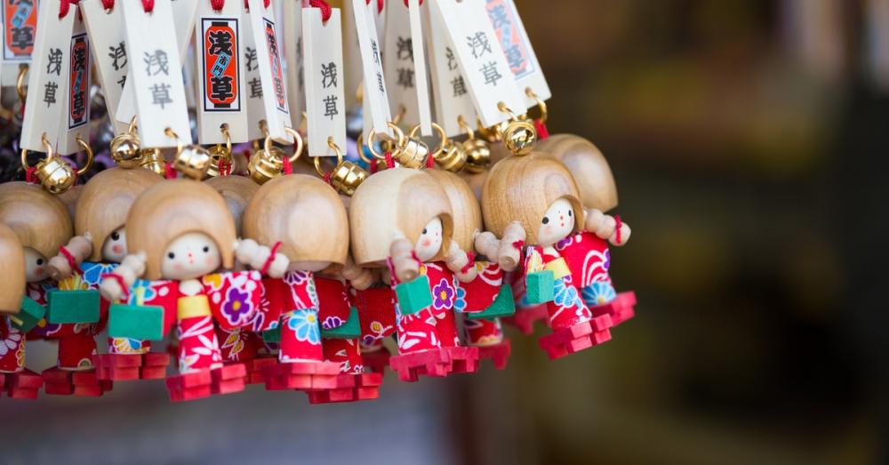 Multiple wooden doll charms hanging in a cluster. They have golden bells and Japanese tags attached to a string.