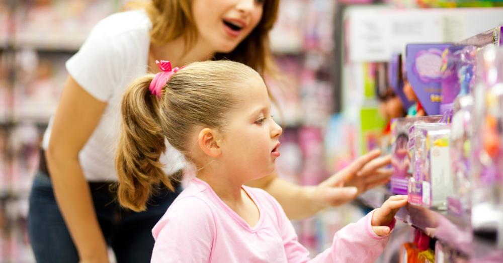 A mom and her daughter looking at toys stocked in the aisle of a store. The toys are in plastic and cardboard boxes.