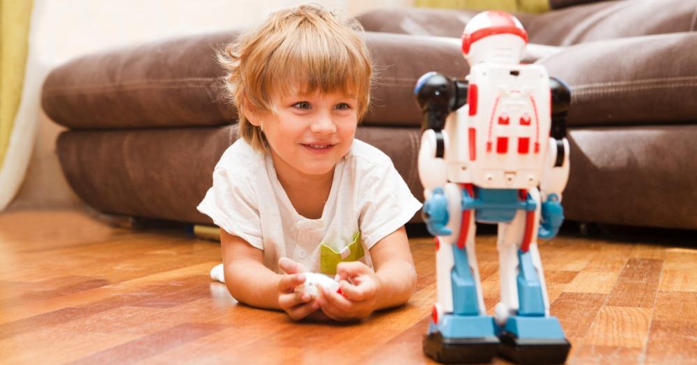A little boy laying on his stomach in his living room. A robotic action figure stands in front of him.