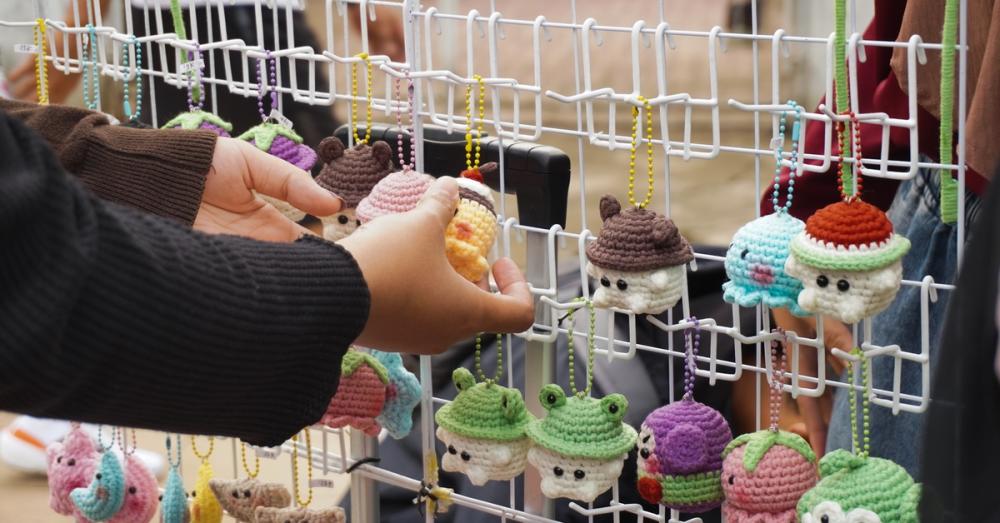 A display of crocheted keychains hanging from a wire rack. There is a hand reaching for one of the keychains.