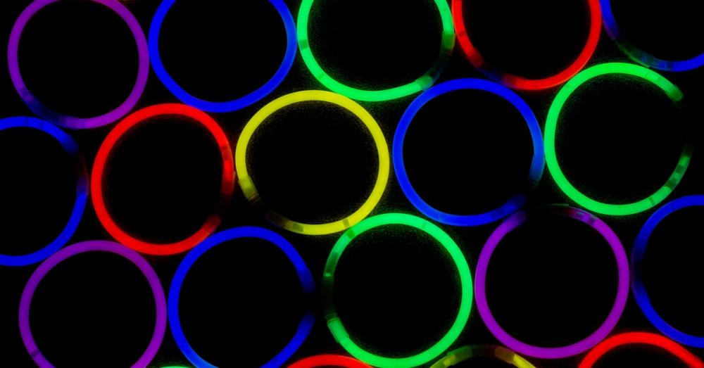 Neon glowing bracelets arranged in a cluster against a black background. They are glowing red, yellow, green, and blue.