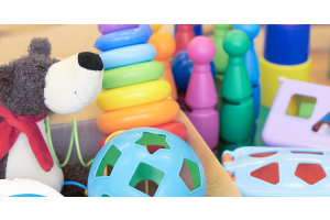 A pile of toys sitting in a cardboard box, including a plushie and a ball. There are more plastic toys outside of the box.