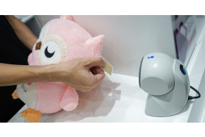 A person using a scanner at a checkout area. They are holding out the tag of a stuffed animal in front of the scanner.